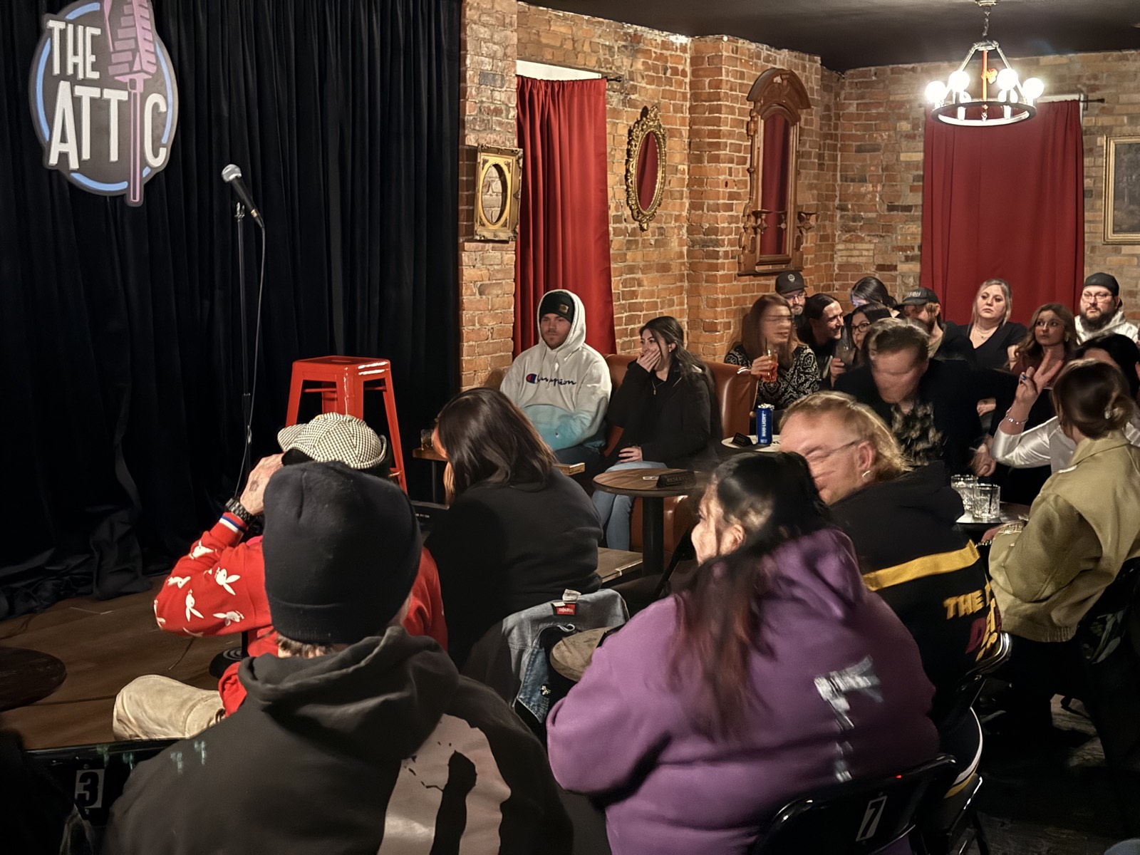 A packed audience at The Attic Comedy Club in Columbus, with the stage, brick walls, and gold frames